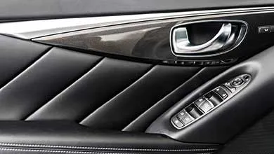 Close-up of a black leather car door panel with diagonal quilting, a chrome handle, and silver armrest controls.