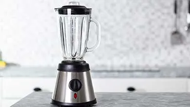 Stainless steel blender with glass pitcher on a dark countertop.