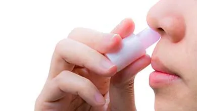 Close-up of a person inserting a white nasal inhaler into their nostril.