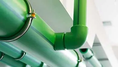 Close-up, low-angle view of green industrial pipes secured to a white ceiling with metal clamps.