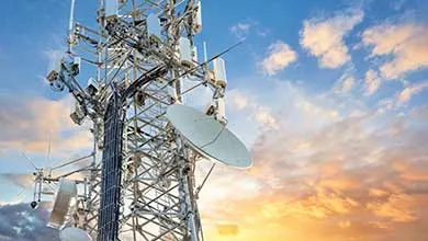 A telecommunications tower with antennas and satellite dishes silhouetted against a vibrant sunset sky.