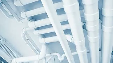 Low-angle view of a ceiling with an intricate network of white pipes.