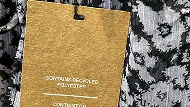 Close-up of a brown paper tag on patterned clothing, labeled "Contains recycled polyester."