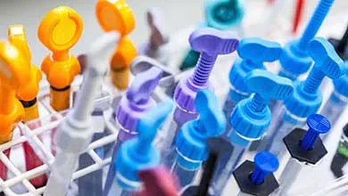 Close-up of laboratory dropper bottles with yellow, orange, purple, and blue bulb tops in a white plastic rack.